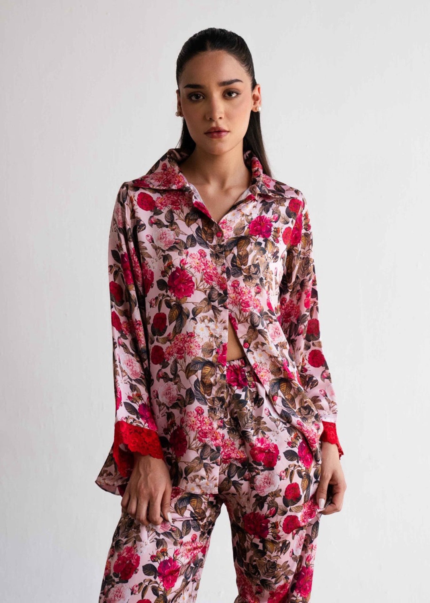 A woman wearing a floral print silk sleepwear set, consisting of a button-up shirt and matching pants.