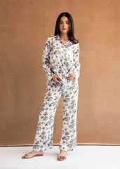 A female model wearing a matching pajama set with a tropical palm tree print on white silk fabric. The set includes a button-down shirt and coordinating pants.