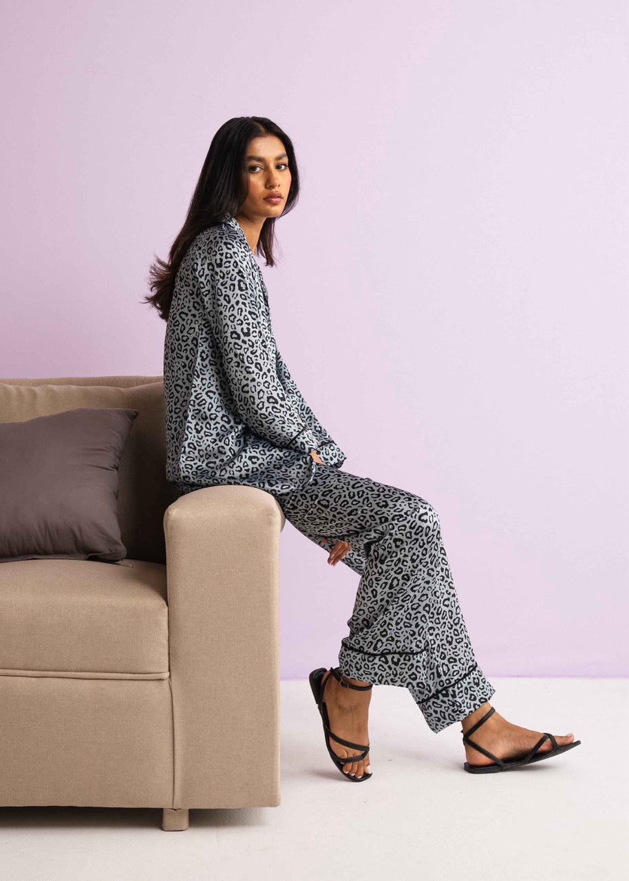 A woman sitting on a chair wearing a leopard print pajama set with a button-down shirt and matching pants.