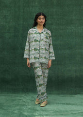 A women wearing a green silk pajama set with floral prints, consisting of a button-down shirt and matching pants.