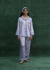 A woman wearing a baby blue silk pajama set with flamingo prints, consisting of a button-down shirt and matching pants. - Larosa pak