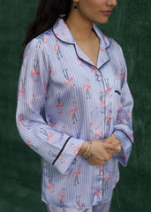 A woman wearing a baby blue silk pajama set with flamingo prints, consisting of a button-down shirt and matching pants. - Larosa pak