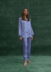 A woman standing and wearing a blue silk pajama set with a mix of striped patterns and polka dots.