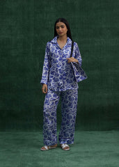 A woman wearing a blue silk pajama set with a leaf print, consisting of a long-sleeved top and pants, larosa