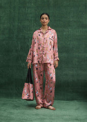 A woman wearing a pink silk pajama set with dog prints, standing against a green background.
