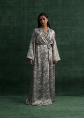 A model wearing a light gray silk gown with floral prints and a matching waist belt, standing against a green background. - Larosa