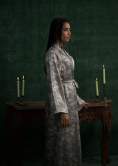 A model wearing a light gray silk gown with floral prints and a matching waist belt, standing against a green background. - Larosa