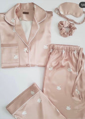 Pink satin pajama set with matching eye mask and hair tie on a light gray background